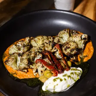 Grilled cauliflower over romesco sauce with chiles and yogurt on a black plate